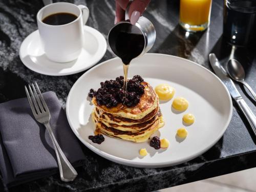 a plate of pancakes with syrup and raisins and a cup of coffee at Kimpton Claret Hotel by IHG in Denver