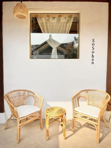 two wicker chairs and a stool next to a window at Jeonju Sosohanhanok in Jeonju