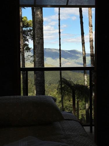 a bedroom with a large window with a view of the mountains at Chalé Portal Villas 03 in Monte Verde