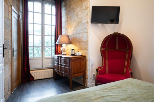 a bedroom with a bed and a red chair and a window at Hôtel La Couleuvrine Sarlat Centre Ville in Sarlat-la-Canéda