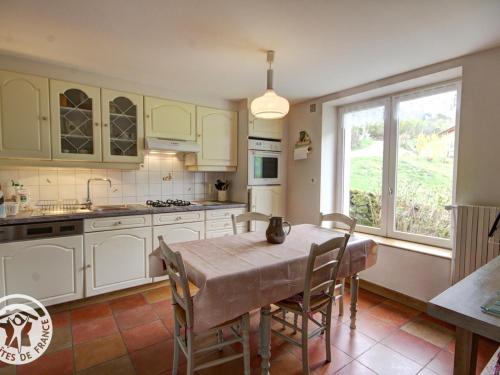 une cuisine avec des armoires blanches et une table avec des chaises dans l'établissement Gîte rural familial avec jardin, terrasse et équipements modernes près du Parc Livradois Forez - FR-1-496-22, à Chérier