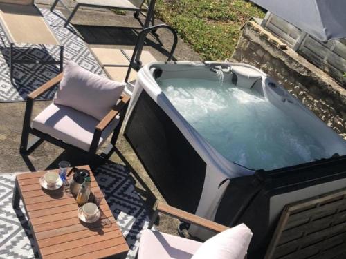 a hot tub on a patio with a chair and a table at Gîte cosy avec spa, grand jardin, proche de la rivière Sioule - idéal pour famille et relaxation - FR-1-489-342 in Saint-Bonnet-de-Rochefort