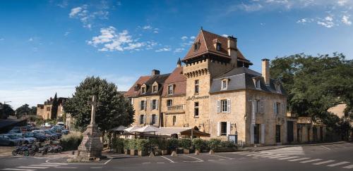 a large brick building with a tower on a street at Hôtel La Couleuvrine Sarlat Centre Ville in Sarlat-la-Canéda