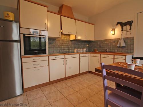 a kitchen with white cabinets and a table and a refrigerator at Maison familiale avec jardin clos près du Haras National du Pin - FR-1-497-173 in Le Merlerault