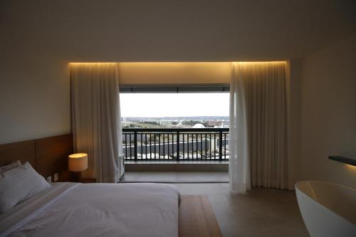 a bedroom with a bed and a large window with a balcony at Conforto e Vista Panorâmica com Banheira Hotel Vision TV WiFi Ar Cond e Cozinha in Brasilia