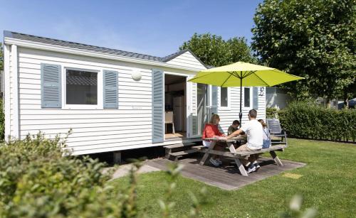 a man and woman sitting at a picnic table under an umbrella at Vakantiepark Klein Strand - Comfort Chalet 4p in Jabbeke