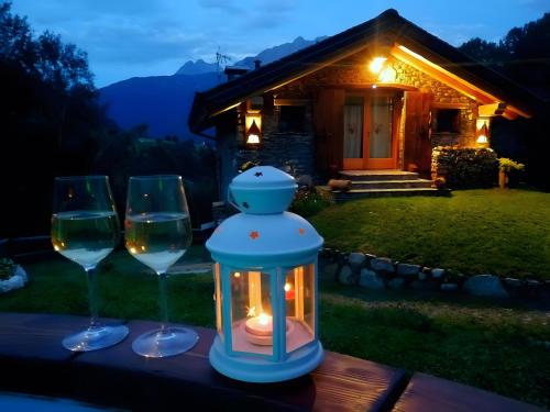 two wine glasses and a lantern on a table in front of a house at Camera Deluxe - Cuore Selvatico in Monno
