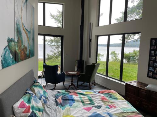 a bedroom with windows and a bed and a table and chairs at Cokely Cove Guesthouse - Oceanside Villa in Denman Island