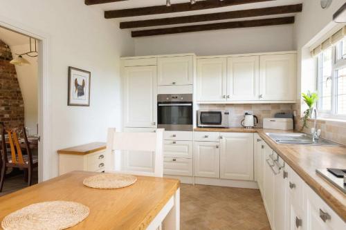 a kitchen with white cabinets and a wooden table at Homely Cottage for 6 Near Chichester & Goodwood in Chichester