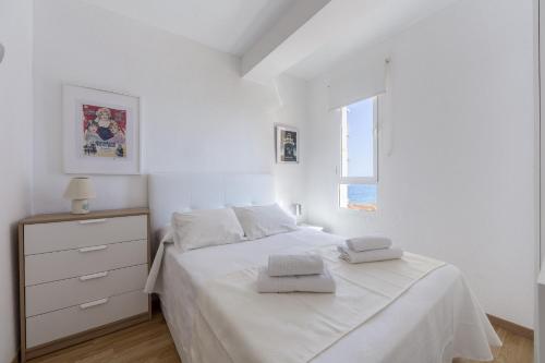 a white bedroom with a white bed and a window at AlmeriaSuite Las Caracolas Beach in Almería