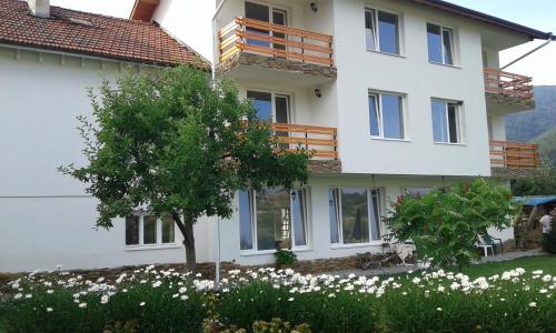 a large white house with a tree and flowers at Atanasovata Kashta in Govedartsi