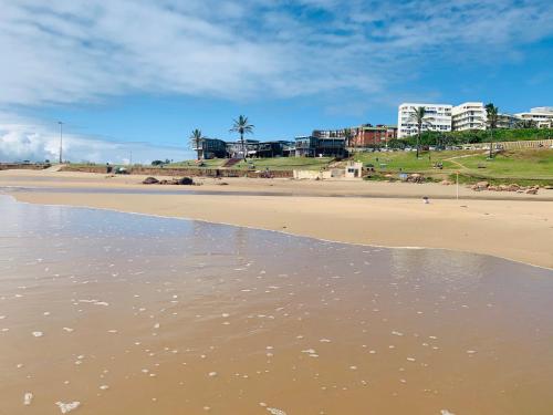a sandy beach with buildings in the background at Coastal Bliss Retreat Peacehaven 207 in Scottburgh