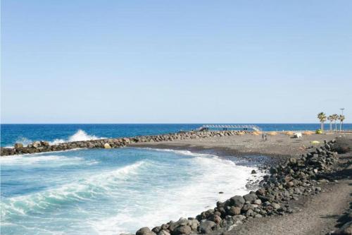a beach with rocks and the ocean and palm trees at Live Candelaria Alsaca con Balcón y Vista al Mar in Candelaria