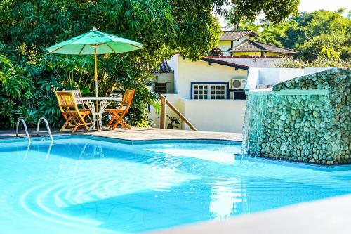 a swimming pool with a table and an umbrella at VELINN Pousada Bromelias in Ilhabela