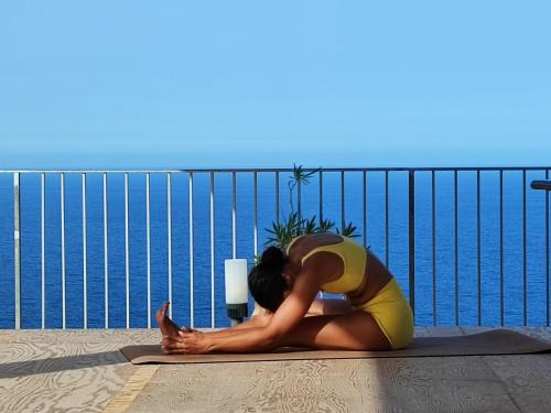 a woman sitting on a yoga mat on a balcony at Hotel Antica Cascina Del Golfo in Scopello