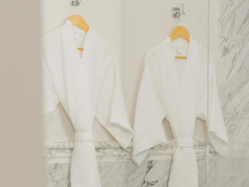 three white sweaters hanging on a rack in a bathroom at Hotel Maria Camille in San Miguel de Allende