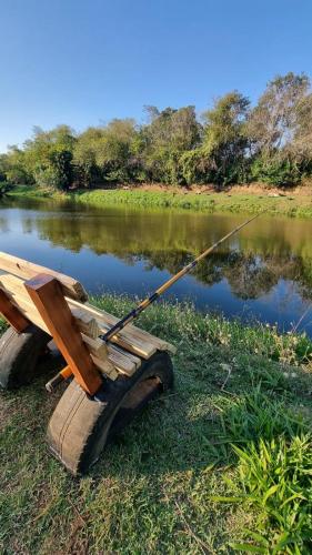 a wooden bench with a fishing rod next to a lake at Chalé do Lago in Pirapitingui