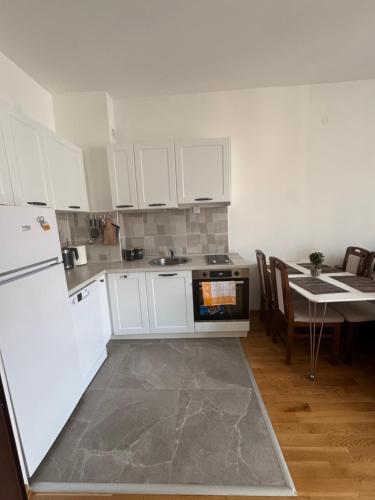 a kitchen with white cabinets and a table and a refrigerator at Blue wave apartman in Becici