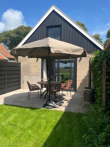 una mesa y sillas bajo una sombrilla en un patio en Muziekskuur, en Hollum