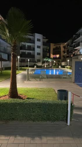 a palm tree and a swimming pool at night at Cosy apartment in Bouznika in Bouznika