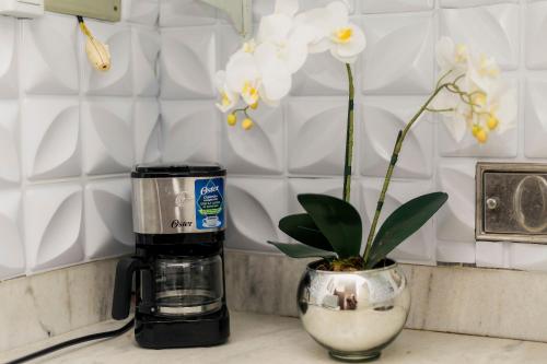 a coffee maker sitting next to a vase with white flowers at Suíte no Centro de Caxambu - Poucos metros do Parque in Caxambu