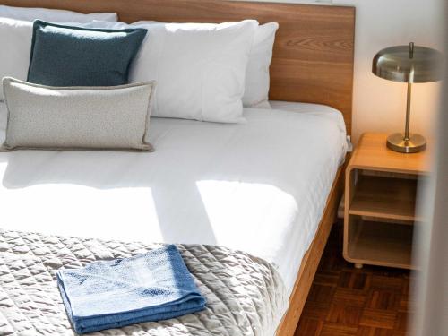 1 cama con sábanas blancas, almohadas azules y lámpara en Prickly Pear Stays in Mayfield West, en Minmi