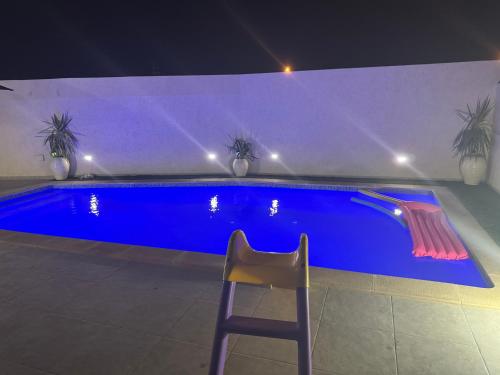 a chair sitting next to a blue swimming pool at night at Villa Lamys Djerba Houmt Souk à 5 minute du centre ville in Al Hara Al Kabira