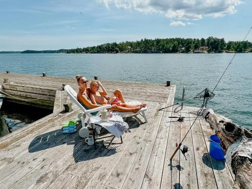 two women sitting on a dock on a lake at Serene Waterfront Oasis Your Resarö Sanctuary in Vaxholm