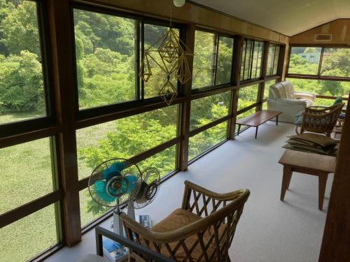 a living room with large windows looking out at the forest at わくわく自然体験の宿ゲストハウス山楽 in Itoigawa