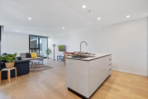 a white kitchen and living room with a couch and a table at Sleek 1-Bed Canberra Flat with Gym & Sauna Access in Canberra