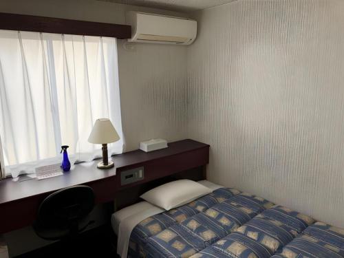 a bedroom with a bed and a desk with a lamp at Hotel Town Nishikigawa in Kochi