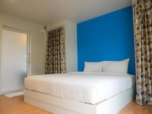 a bedroom with a large white bed with a blue wall at Baan Kula Mahasarakam in Maha Sarakham