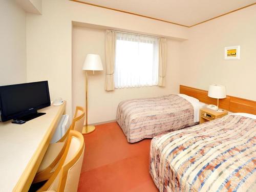 a hotel room with two beds and a desk with a television at Hotel Grand Shinonome in Tsukuba