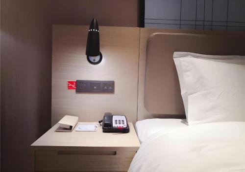 a bedroom with a bed and a phone on a night stand at Echarm Hotel Changde Taoyuan Walking Street Jinyuan Tower in Changde