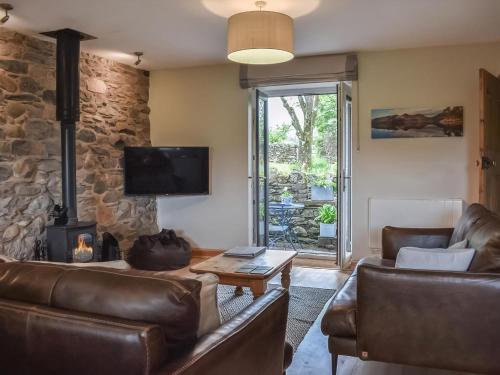 a living room with leather furniture and a stone wall at 1, The Barns in Threlkeld