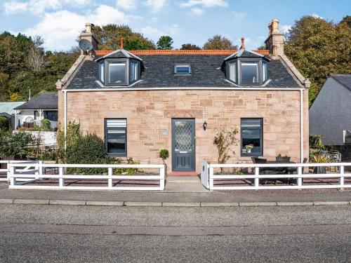une maison en briques avec une clôture blanche devant elle dans l'établissement Shore View Cottage, à North Kessock