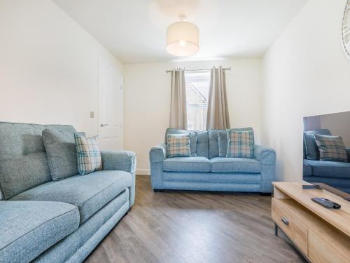 a living room with two blue couches and a tv at Silkstone Crescent in Buxton