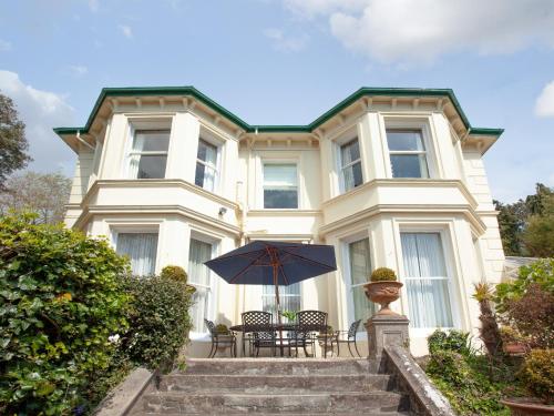 a house with a table and an umbrella in front of it at Longcroft House in Torquay