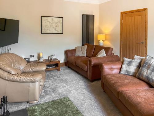 a living room with leather furniture and a flat screen tv at Inveravon Cottage in Polmont