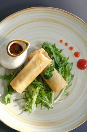 a white plate with a sandwich and greens on it at Aster Apartment Bali in Canggu