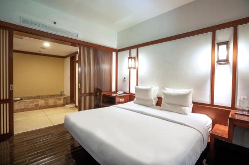 a bedroom with a large white bed and a bathroom at Novotel Bogor Golf Resort in Bogor