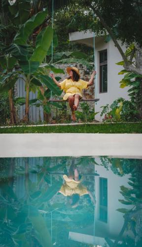 a woman in a yellow dress sitting on a swing next to a swimming pool at Casa Cactus Buenavista in Bacalar