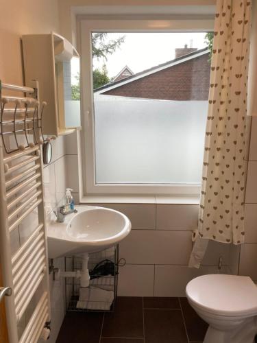 a bathroom with a sink and a window and a toilet at CUXKieker - Moderne Ferienwohnung mit Pep in Cuxhaven-Sahlenburg, WLAN, Parkplatz und Gartenblick, nah am Nordseestrand und Wernerwald in Cuxhaven