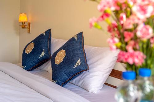 a bed with blue and white pillows and a vase of flowers at Tràng An Sunny River Homestay in Ninh Binh