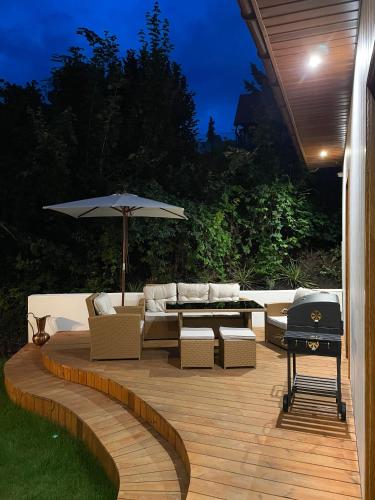 a patio with a couch and an umbrella and a grill at Zloty, a Skromny - ogrodzony domek z jacuzzi i widokiem na jezioro in Górzno