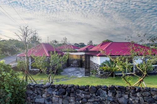 a house with red roofs and a stone wall at Juwoldam in Jeju