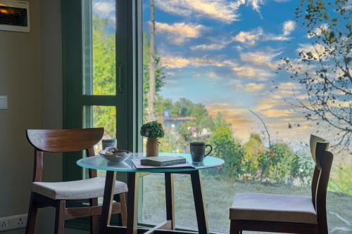 a table and two chairs in front of a window at SaffronStays Edelweiss Estate Amore in Chaubattia