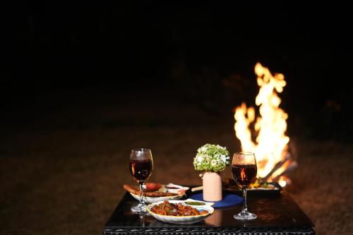 a table with two glasses of wine and a fire at SaffronStays Edelweiss Estate Amore in Chaubattia
