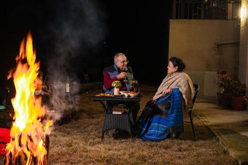 two people sitting at a table next to a fire at SaffronStays Edelweiss Estate Amore in Chaubattia