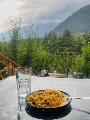 a plate of pasta and a glass of water on a table at The Highgrove House, Manali in Haripūr
